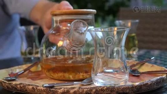 一个人把热茶从玻璃茶壶倒入一个透明的杯子里。 草药茶视频