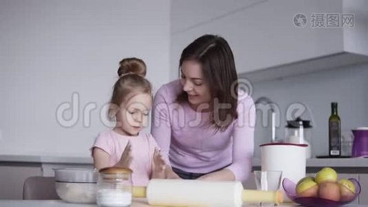 可爱的小女孩和她漂亮的妈妈在厨房里揉面团的时候玩得很开心，笑得很开心。 女孩触摸视频