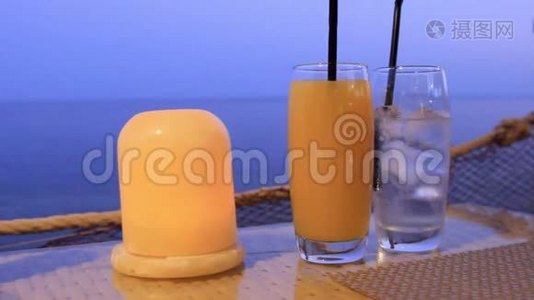 在岸边的一张桌子上的一个酒吧里，站着两只玻璃杯，里面有鸡尾酒和一支燃烧的蜡烛视频