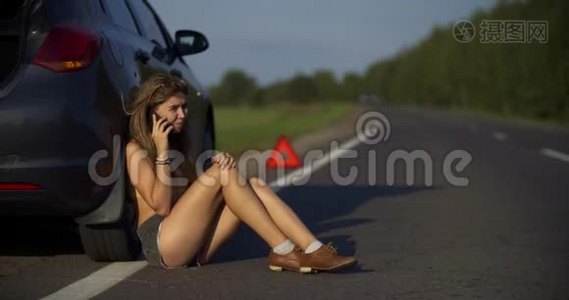 一个年轻的女人看着电话里的东西，一辆破车在路上的车架上紧急视频