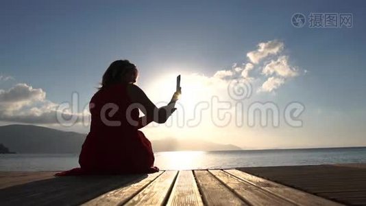 一个女人坐在海边，慢镜头地拍着日出时的景色视频