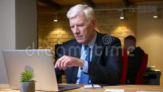 一位老白种人商人用笔记本电脑在办公室工作时在室内做笔记的特写镜头视频