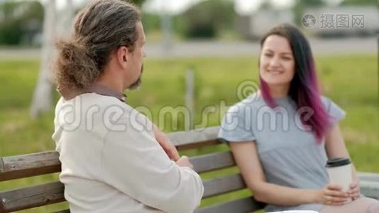 一位轻松迷人的中年男子，长发灰白，一位染发的年轻女子坐在公园的长凳上。视频