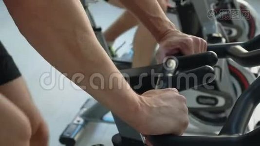 在健身室里，男性手拿室内自行车。 人在健身房的自行车课上旋转自行车。 健身男子训练视频