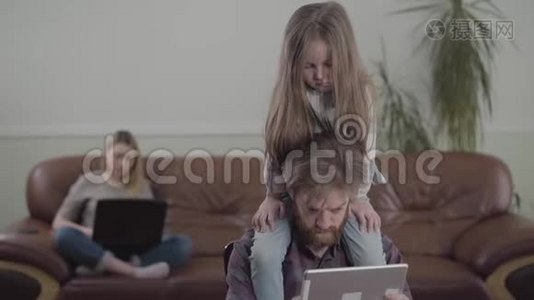 有胡子的人用平板电脑特写的肖像。 悲伤的小女孩坐在父亲的脖子上。 沙发上的妈妈视频