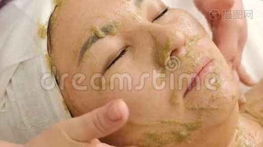一个穆斯林女孩在美容院的复健程序。 面部和颈部按摩用海藻滋养面膜。 特写镜头。 双手视频