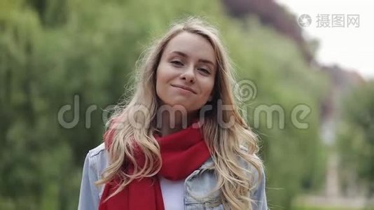 站在城市公园外面戴着红领巾的年轻美女的肖像。 美丽的女人微笑着看着视频