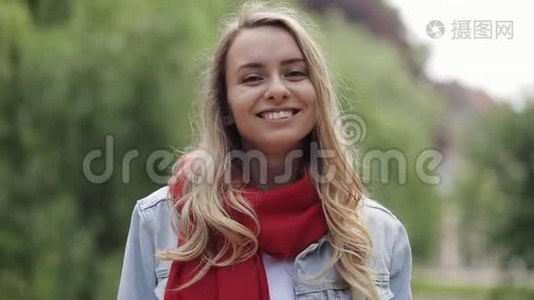 年轻漂亮的女人笑着，快乐地享受着积极的生活方式，戴着红领巾站在公园里。 关闭视频
