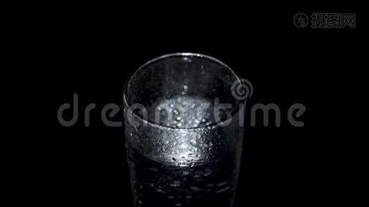 一杯湿漉漉的水在黑暗中旋转，闪烁着光视频