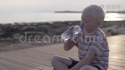 一个金发男孩从瓶子里喝水。视频