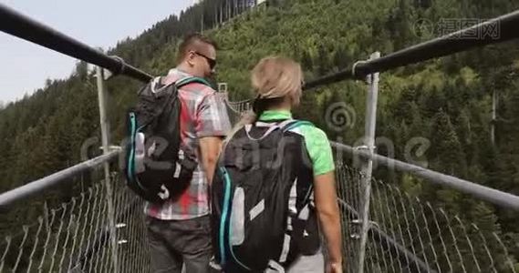 一男一女背着背包正沿着山里的一座长长的吊桥走着..视频