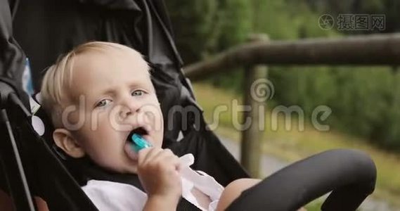 一个可爱的男孩坐在婴儿车厢里，吮吸一根棒棒糖。视频