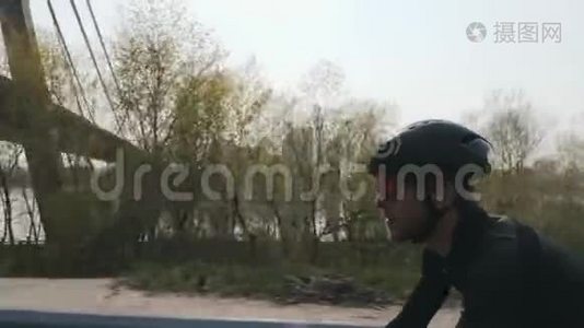 骑自行车的骑自行车者的特写镜头。 带着黑色头盔和墨镜骑着自行车骑着桥和河视频