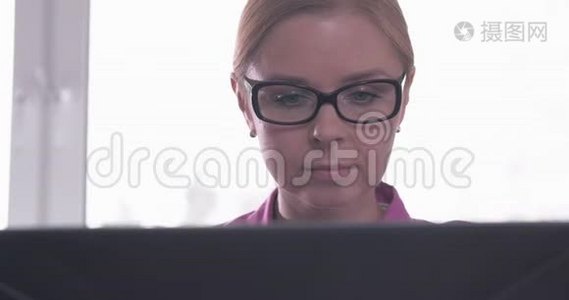 戴眼镜的微笑女人在笔记本电脑上工作的肖像视频