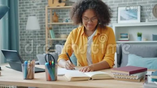微笑的年轻女子在办公桌上写着笔记本，在家工作视频