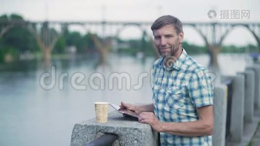 夏天，成熟的男人在河边的码头上浏览数字平板电脑视频