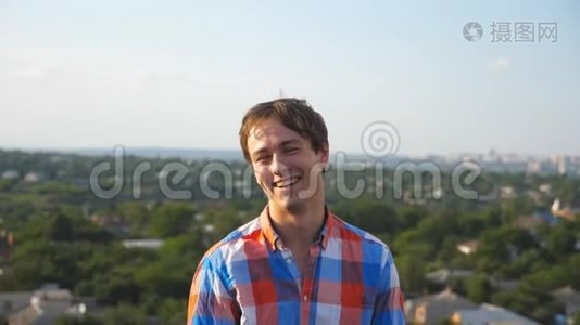在城市景观背景下坐在屋顶上的年轻快乐男人的肖像。 英俊的家伙笑着，露出喜悦的表情视频