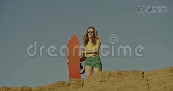 沙漠里有沙板的性感女孩。 体育，旅游，生活方式，商业，广告概念。 拍摄于4k红色视频