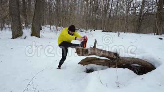 穿着黄色外套的蓄须运动员在冬天的森林里雪天伸腿视频