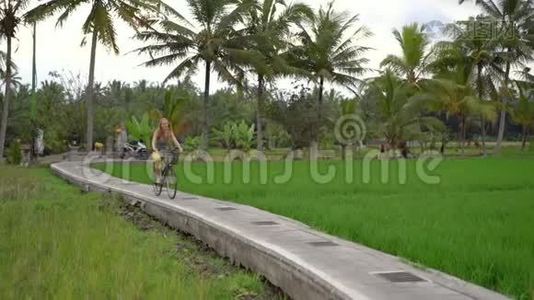 一个年轻的女人骑着自行车穿过美丽的稻田。 前往东南亚的概念。 慢镜头视频