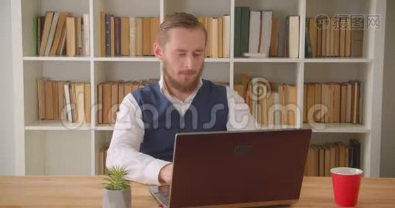 年轻成功的高加索商人用笔记本电脑在办公室室内喝咖啡的特写镜头视频