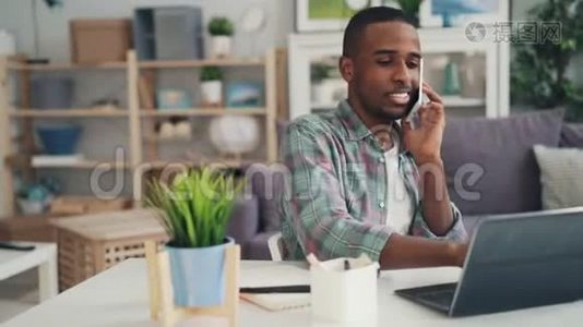 年轻的非裔美国人专家在手机上和商务人士交谈，笑着用笔记本电脑工作视频