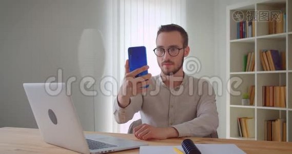 年轻英俊的白种人商务明星坐在笔记本电脑前用手机自拍的特写照片视频