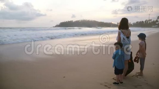 后景，快乐的年轻母亲和两个孩子一起在异国情调的热带海滩观看令人难以置信的大气日落。视频