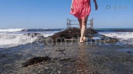 年轻的美女赤脚走在海上码头上，海浪拍打着码头。 腿靠近视野。 慢动作视频