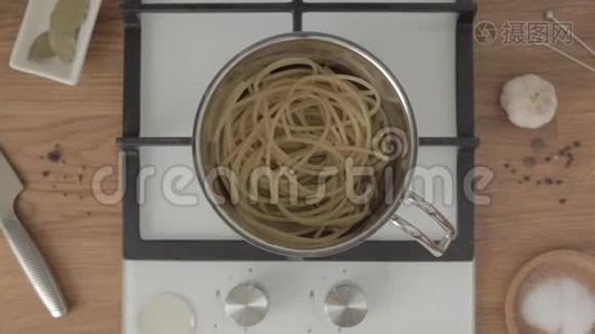 手把半勺油放在金属锅里，煤气炉上放着煮好的意大利面视频