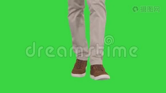 穿着米色牛仔裤和棕色运动鞋在绿色屏幕上行走的男人的脚，Chroma键。视频