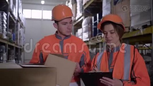 两名员工穿着工作服，戴着头盔，在仓库附近的箱子里讨论工作视频