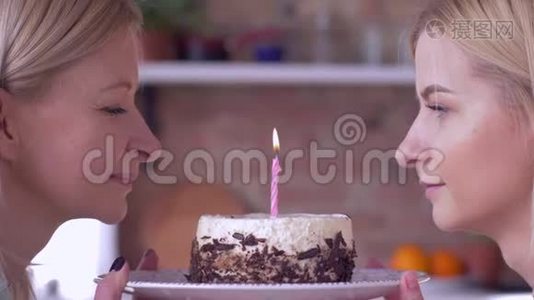 祝你生日快乐，妈妈和成年女儿一起在节日蛋糕上吹蜡烛，微笑着互相看着视频