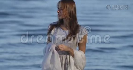 一位思想深邃的白种人女人站在海浪的背景上，穿着浅白的裙子。 有魅力的女孩视频