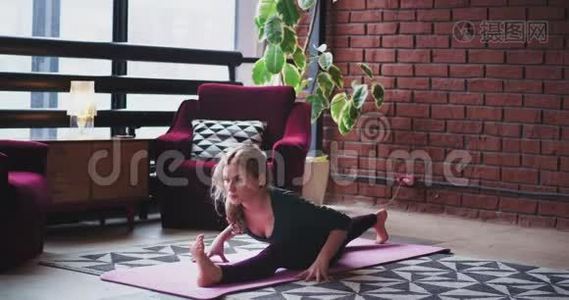 早晨，年轻的女士在家里伸展身体，她在客厅的垫子上做瑜伽姿势，有现代的设计和视频