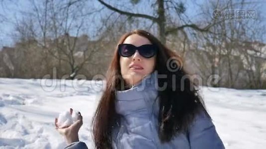 户外女画像美丽的成年女孩戴着深色太阳镜在公园的蓝天背景下玩雪球视频