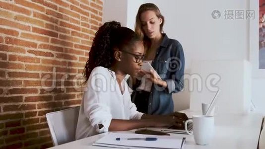 两位年轻漂亮的商务女性在办公室里和数码平板电脑和笔记本电脑一起工作视频