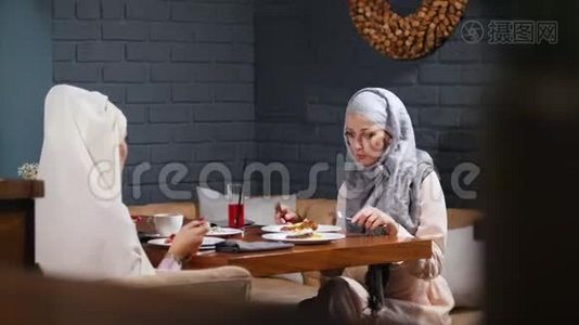 一个穆斯林女人坐在咖啡馆里吃着他们的菜，在谈话视频
