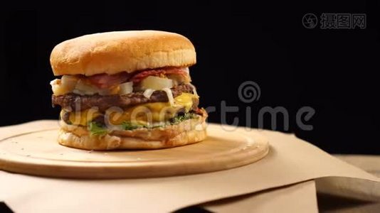 汉堡，有牛肉，奶酪和蔬菜在木板上旋转。 黑色背景视频