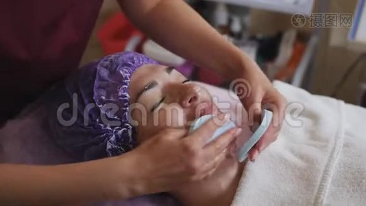美容师在停用抗衰美容面膜后擦拭患者面部..视频