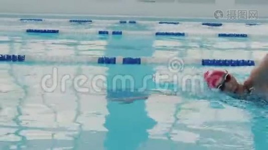 镜头跟随强壮的女游泳运动员在游泳池里。 她穿着泳衣、泳帽和五颜六色的护目镜游泳。 她是视频