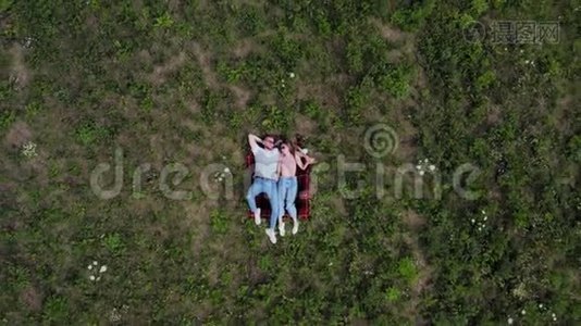 幸福的年轻夫妇躺在草地上。 摄像机慢慢地从他们身边飞走了。 从高空向下。 4K.视频