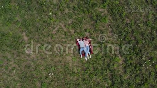 幸福的年轻夫妇躺在草地上。 摄像机慢慢地从他们身边飞走了。 从高空向下。 4K.视频