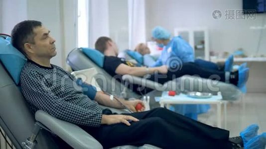 献血者坐在椅子上，手里抽着血。视频