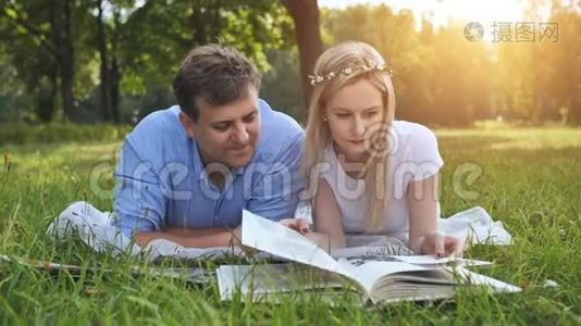 一个男人和一个女孩正在看一张家庭相册，里面有草地上公园里的照片。视频