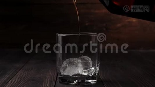 豪华威士忌。 手把金色的威士忌从一个方形的瓶子倒入一个玻璃杯，在桌子上的背景上有真正的冷冰。视频