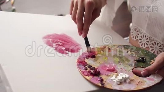 特写女孩用画笔和手指在画布上画粉红色的花。视频