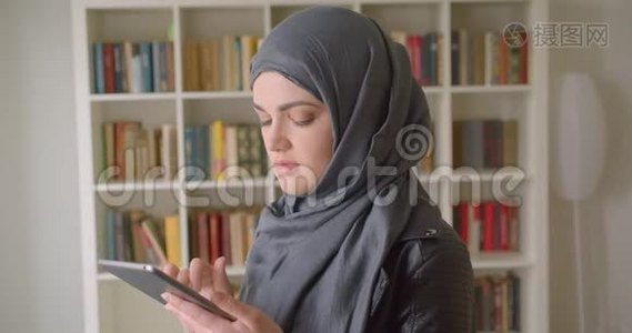 年轻漂亮的穆斯林女学生戴着头巾的特写照片，用平板电脑微笑着看着镜头视频