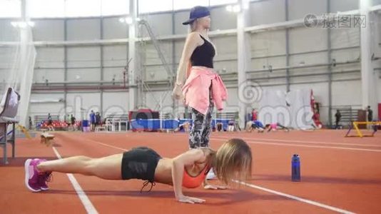 年轻健康的运动女性穿着运动服做俯卧撑。 另一个腿上的女人在蹲视频