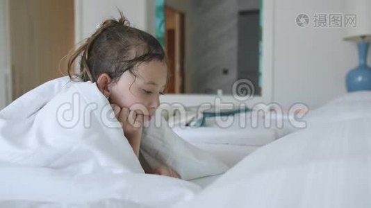小女孩躺在毯子下，在平板电脑上看动画片。视频